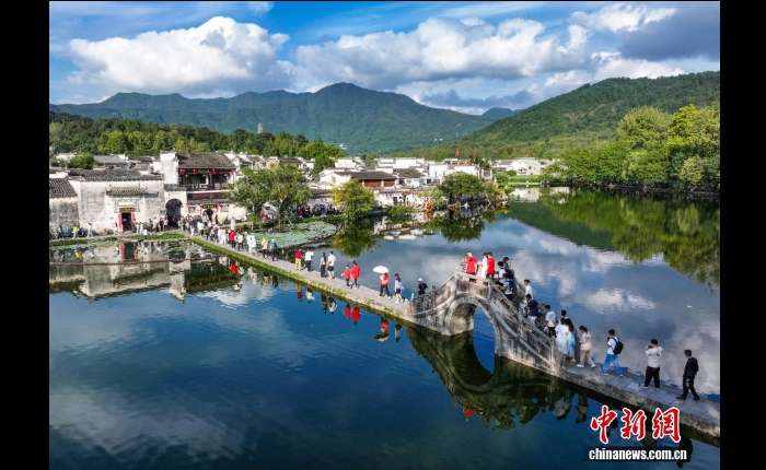 10月1日，国庆长假首日，世界文化遗产地安徽省黄山市黟县宏村迎来旅游热。典雅的徽派建筑与灵动水乡相映成趣，尽显古村魅力。图为游客在宏村游玩赏景。（无人机照片）